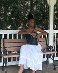 Woman sitting on a bench outdoors, wearing a black top and white skirt.