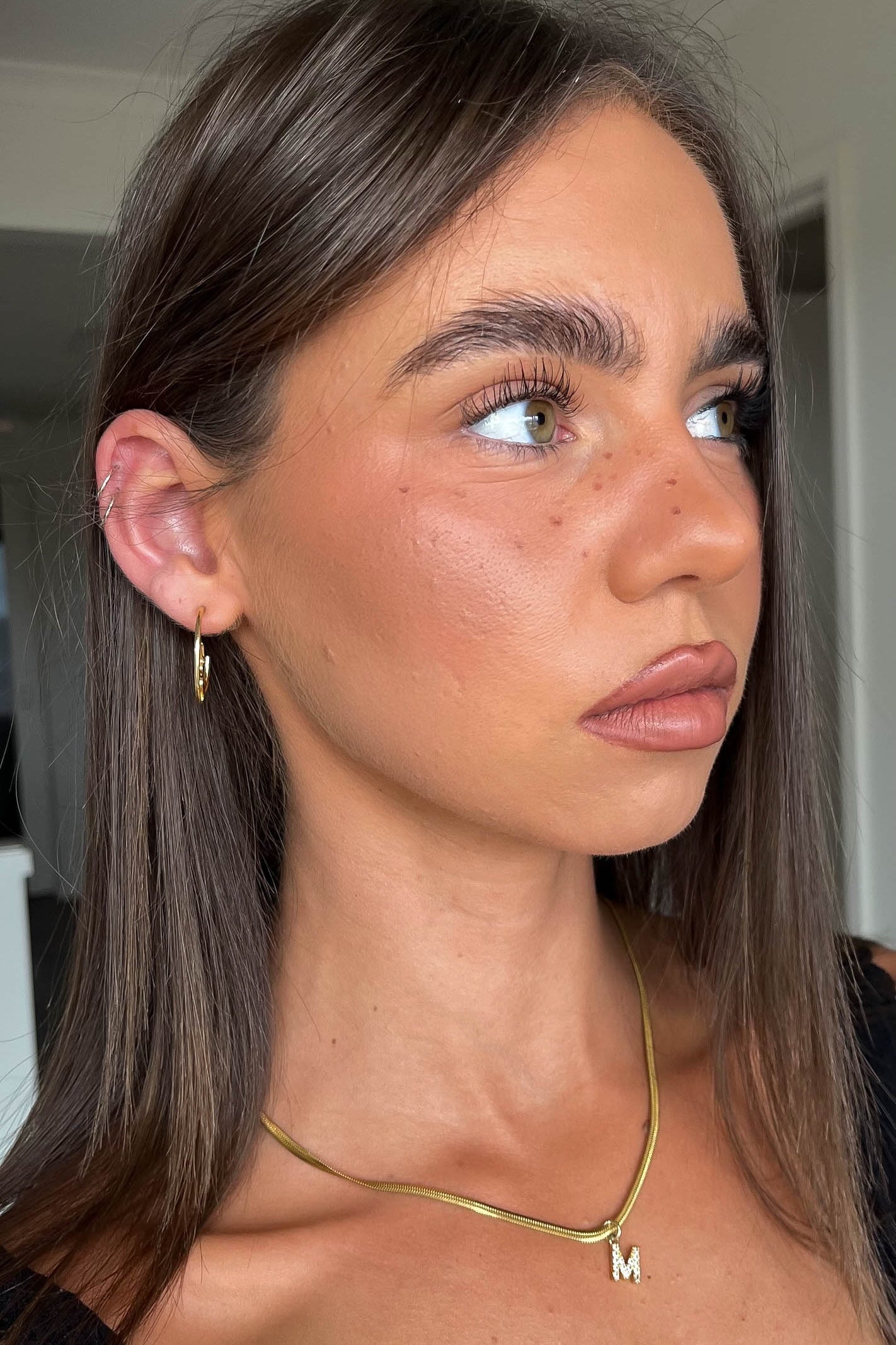 Close-up of a person with long brown hair wearing a gold necklace and earring.
